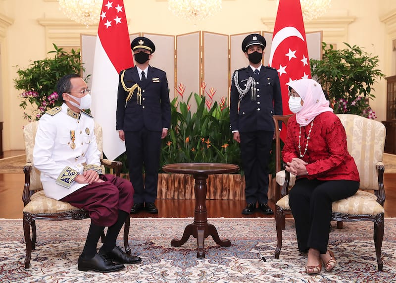 President Halimah Yacob of Singapore meets with a man in formal attire, flanked by guards and Singapore flags.